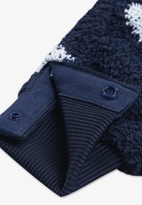 Puño de suéter azul marino con tejido suave y textura, y ribete acanalado. El cierre incluye un botón de presión del mismo color azul marino.