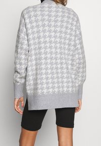 Maglione grigio chiaro a maglia con motivo a zigzag, con polsini e orlo a coste. Vestibilità oversize con spacchi laterali, abbinato a pantaloni corti neri.