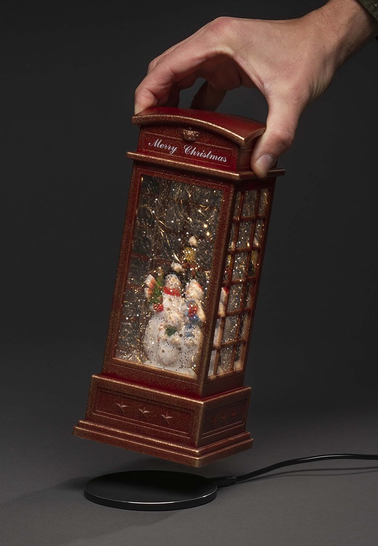 Eine Hand hält eine rote Laterne mit Schneemännern darin, der Text "Frohe Weihnachten" oben und Glitzer wirbelt innerhalb der Laterne.