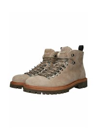 Botas de senderismo de ante marrón claro con ojetes de metal, suelas gruesas marrones, parte delantera con cordones y tiradores negros en los talones, logo en relieve en el lateral.