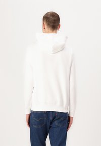 Hvid hættebluse med en glat tekstur. Har ribbede manchetter og kant, kombineret med blå denim jeans. Minimalistisk design.