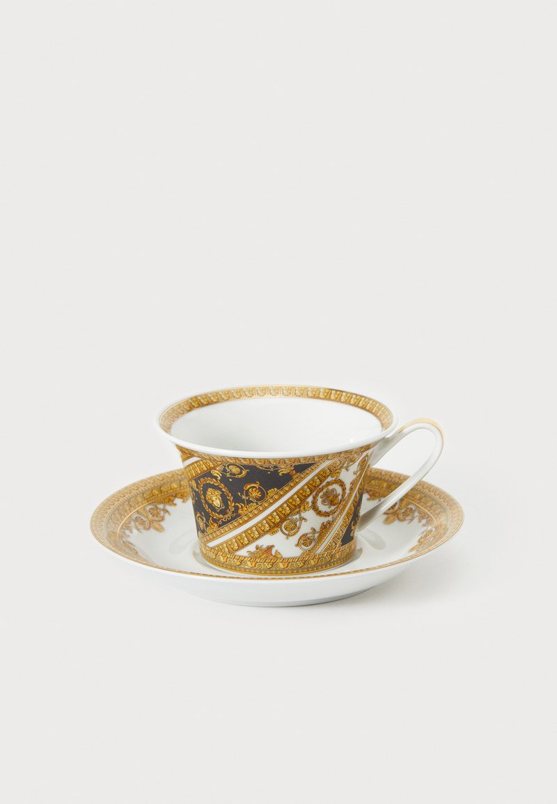 Posliinista valmistettu kuppi ja lautanen; tummansinivalkoinen kuvio, jossa kultaiset koristeelliset yksityiskohdat; sileä pinta, klassinen muotoilu.