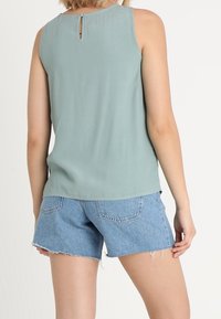 Ljusgrön ärmlös topp med ett nyckelhål bak, kombinerad med blå denimshorts med fransar och bakfickor.