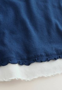 Tissu tricoté en couches bleu et blanc avec bords froncés et festonnés, montré en gros plan.