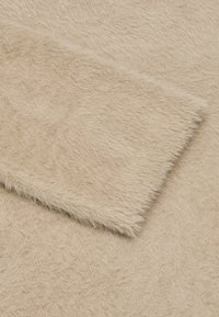 Beige Kunstfellstoff mit einer weichen, strukturierten Oberfläche, die unterschiedlich lange Fasern und einen glatten, kürzerhaarigen Abschnitt aufweist.