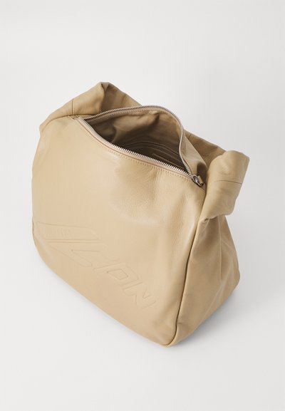 Beige nahast kott, millel on lukuga sulgemine ja pehme tekstuur. Omab voltimisega disaini ning reljeefset logo detaili külgedel.