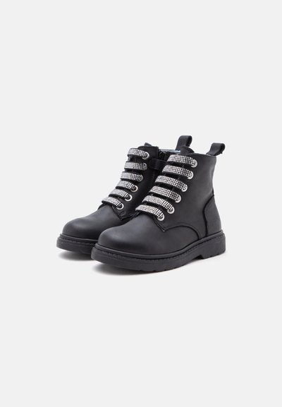 Paire de bottines noires avec semelles épaisses et lacets larges argentés brillants ornés de cristaux sur un fond clair uni.