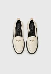 Kreemikaalised loafersid läikiva patendiga, must kummist tallaga ja kuldse tooni logo aktsendiga vampi peal. Tekstuuriga sisetald.