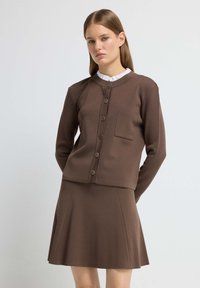 Brown two-piece outfit featuring a fitted long-sleeve top with a round neckline and button closure, paired with a flared skirt.