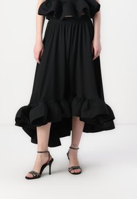 Jupe noire évasée avec un ourlet froncé, fabriquée en tissu doux. Assortie à des sandales à talons hauts noires avec des brides, ornées d'accents en strass.