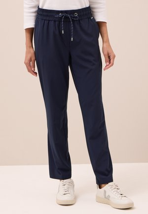 Jogging bleu marine avec une taille élastique et un cordon de serrage, présentant une texture lisse et un design fuselé. Portés avec des baskets blanches.
