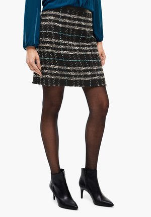 Vrouw die een zwart-witte gestreepte tweed minirok draagt, doorschijnende zwarte panty's, zwarte enkellaarsjes met hakken en een blauw blouse met lange mouwen.
