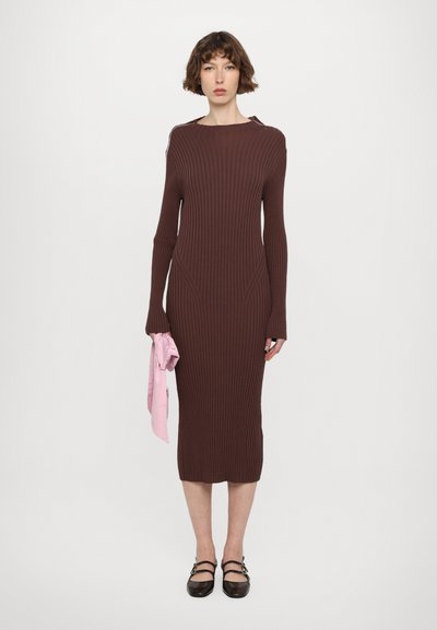 Rochie tricotată maro cu dungi, cu mâneci lungi și o siluetă ajustată, având cusături laterale și un guler înalt. Accesoriu: o panglică din material roz, legată manual.