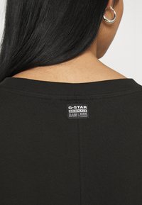 Czarna bawełniana koszulka z okrągłym dekoltem, widocznymi szwami i metką z napisem "G-Star Originals RAW Denim" z tyłu.