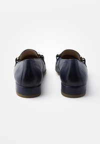 Scarpe in pelle blu navy con tacco basso, caratterizzate da dettagli in metallo dorato e una texture liscia. Sul retro si notano semplici dettagli di cucitura.