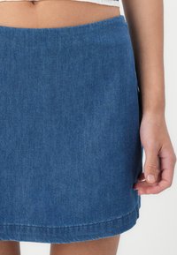 Denimskjørt i mørk blå med en ren finish. Har en enkel silhuett og en lett풀lete kant langs den nederste kanten.