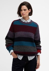 Knit sweater with multiple horizontal stripes in burgundy, teal, gray, and black, featuring a ribbed texture and loose fit. Layered over a collared shirt.