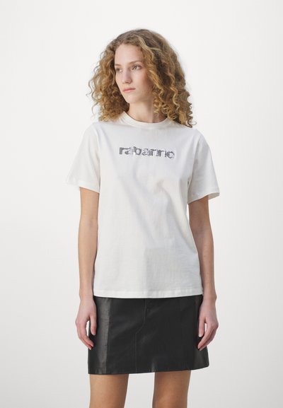 T-shirt en coton blanc à manches courtes, avec un logo texturé "rabanne" en argent. Associé à une mini-jupe en cuir noir.
