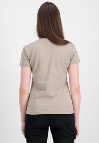T-shirt beige à manches courtes en tissu doux, de forme ajustée et à texture lisse, vu de dos, associé à un pantalon noir.