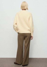 Suéter de punto texturizado color crema, de corte holgado, combinado con pantalones marrones de pierna ancha. El calzado es marrón, plano y ligeramente texturizado.