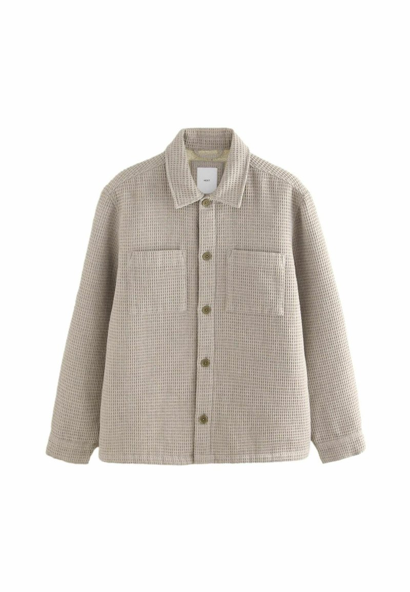Textured beige overshirt with a collar, front pockets, and green buttons. Made from woven fabric with a grid pattern and long sleeves.