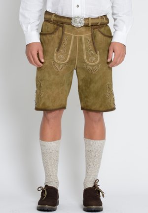 Man draagt traditionele bruine Lederhosen shorts met geborduurde details, beige kniekousen, bruine schoenen en een wit shirt.