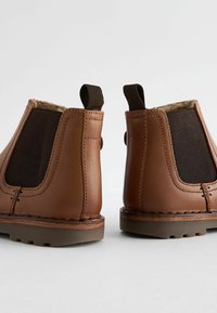 Bruna läderankelboots med elastiska sidopaneler, stickade detaljer och dragflikar bak. Grov gummisula för bra grepp.