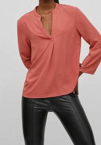 Top di tessuto corallo con placca parziale e maniche a tre quarti, abbinato a leggings neri in pelle a vita alta.