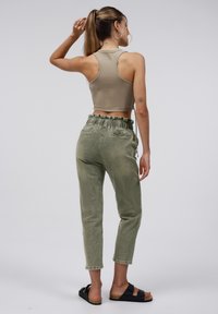 Beige cropped tanktop, groene hoge taille broek met een gerimpelde elastische taille en zwarte slide-sandalen. Glad materiaal met een relaxte pasvorm.