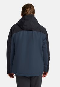 Giacca impermeabile blu e nera con cappuccio, caratterizzata da una texture liscia e blocchi di colore a contrasto sulle spalle e sulla schiena.