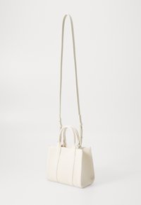 Mała prostokątna torebka z kremowej tkaniny z dwiema uchwytami i długim regulowanym paskiem na ramię, wyeksponowana na jednolitym tle.