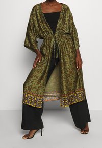 Zielony kimono w wzory z motywem paisley, ściągnięte w talii paskiem, z wyrazistą żółto-czarną bordiurą.