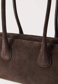 Σκούρα καφέ τσάντα από σουέντ με δύο ανθεκτικές λαβές και απαλή, υφή επιφάνεια πάνω σε απλό φωτεινό φόντο.