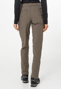 Pantalones caqui para mujer con corte ajustado, que presentan dos bolsillos traseros y una textura de tela suave. Combinados con zapatos de senderismo negros.