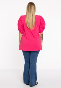 Fuchsia top met pofmouwen van katoen, gecombineerd met blauwe flare jeans. De top heeft een relaxte pasvorm en een ronde zoom.