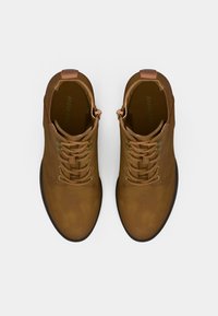 Un par de botines de cuero marrón con puntas redondeadas y cierre de cordones, vistos desde arriba sobre un fondo blanco puro.