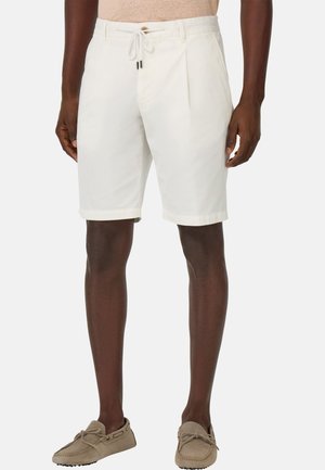 Shorts en coton blanc avec une taille à cordon, un devant plissé et des ourlets roulés, associés à des chaussures de style mocassin gris clair.
