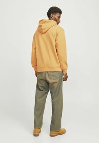 Sweatshirt in lichtoranje, met een capuchon en geribde manchetten. Gecombineerd met vervaagde groene baggy jeans en tan schoenen.