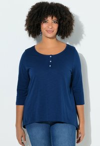 Navyblauw, top met lange mouwen en een ronde hals, drietalige knoopsluiting aan de voorkant en een licht asymmetrische zoom. Zachte stoftextuur.