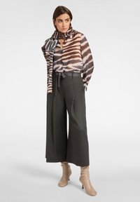 Langearmige blouse met bruine en blauwe abstracte patronen, gecombineerd met hoogwaardig grijze wijde broek en beige enkelhoge laarzen met hak.
