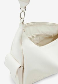 Sac à main texturé blanc avec fermeture éclair, doté d'une poche intérieure, d'une bandoulière réglable et d'un détail de marque subtil.