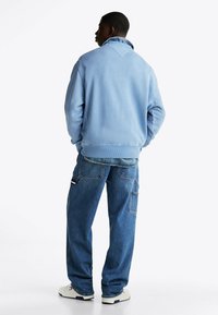 Jasnoniebieska polarowa kurtka z wysokim kołnierzem i elastycznymi mankietami, w połączeniu z luźnymi niebieskimi dżinsami z wieloma kieszeniami.