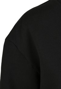 Felpa nera con una texture morbida, con scollatura rotonda e maniche raglan. Il tessuto appare liscio e spesso con una minima cucitura decorativa.