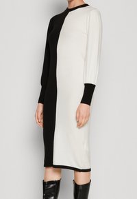 Stickad klänning med en halva svart, halva vit design, långa puffärmar och ribbade muddarna. Slät textur och knälång klipp.