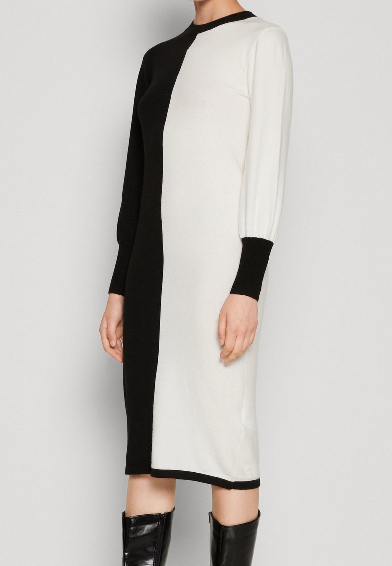 Stickad klänning med en halva svart, halva vit design, långa puffärmar och ribbade muddarna. Slät textur och knälång klipp.