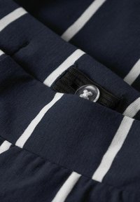 Tessuto navy con strisce orizzontali bianche, dotato di chiusura a bottoni e di una banda elastica nera. Materiale texturizzato con cuciture visibili.