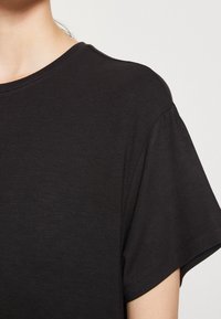 Czarna, krótki rękaw t-shirt wykonany z miękkiego materiału, z klasycznym okrągłym dekoltem i delikatnie luźnym krojem. Gładka tekstura bez widocznych wzorów.