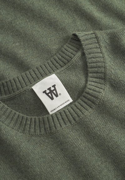 Pull en tricot vert avec un col rond côtelé. Étiquette visible avec le logo et le nom de la marque. Texture douce avec un motif subtil.