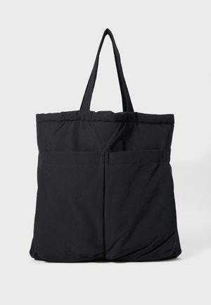 Bolsa tote acolchoada preta com dois bolsos frontais e alças duplas sobre um fundo branco.
