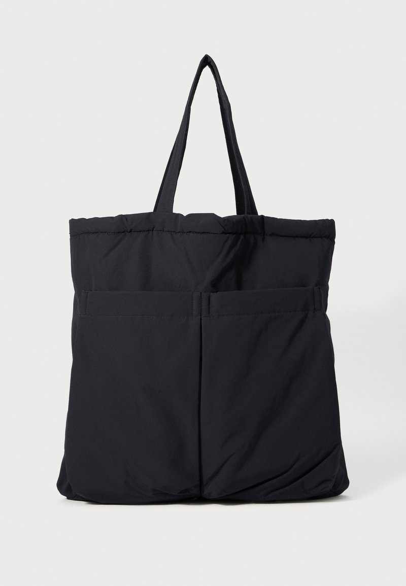 Sac fourre-tout noir rembourré avec deux poches avant et des doubles poignées sur un fond blanc.